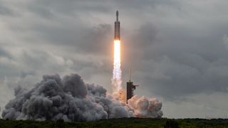 a large white rocket launches into a cloudy gray sky.