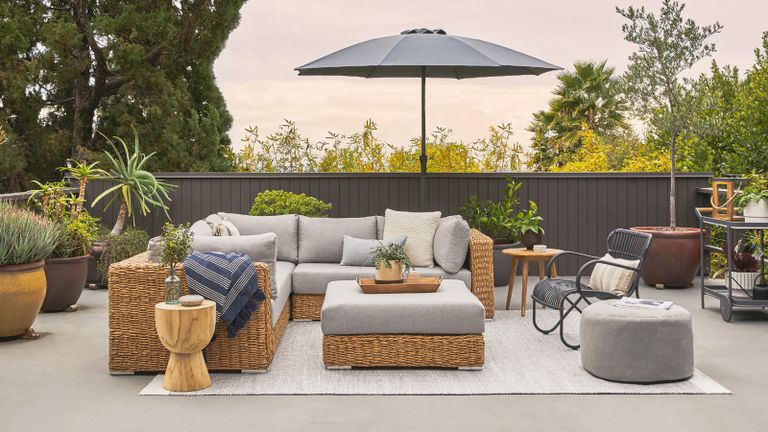 A wicker outdoor sectional sofa and patio furniture with a patio umbrella in a modern backyard