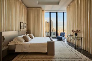 large bedroom with curtains wrapping walls, view of NYC, upholstered bed, and large white rug with black border