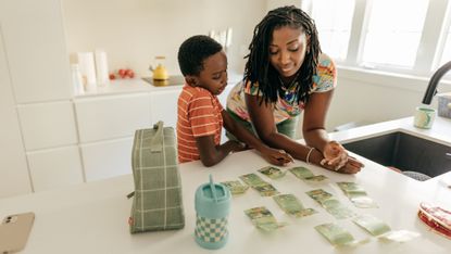 A mom helps her young son learn about money at the kitchen counter.