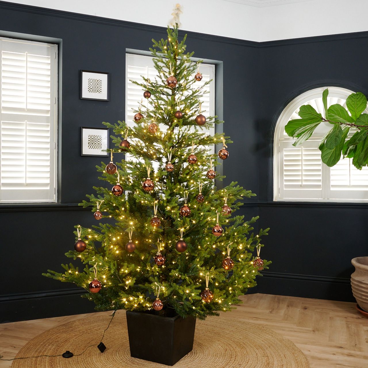 John Lewis Cotswold 7ft Potted Pre-lit Christmas Tree decorated with brown baubles set up in a black-painted living room