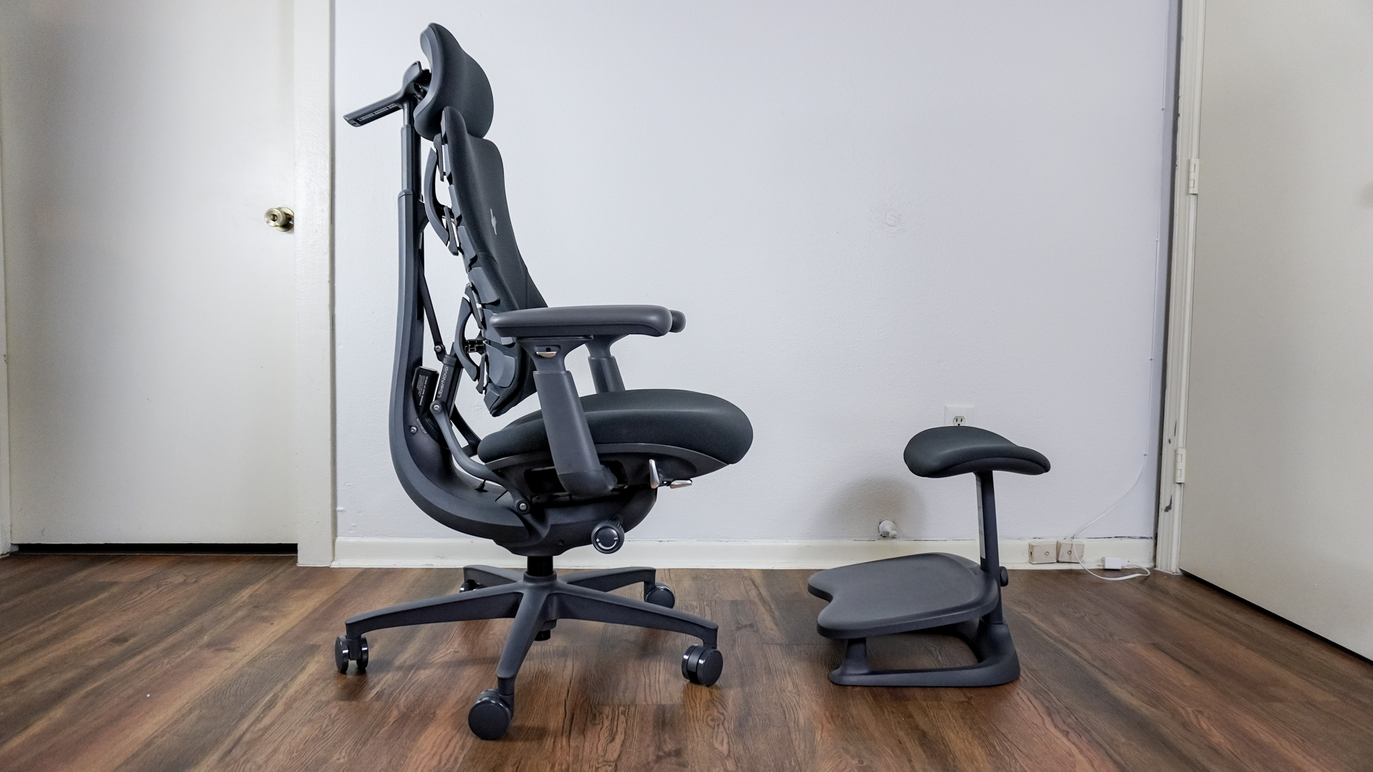 The LiberNovo Omni office chair and its optional footrest up against a wall and viewed from the side