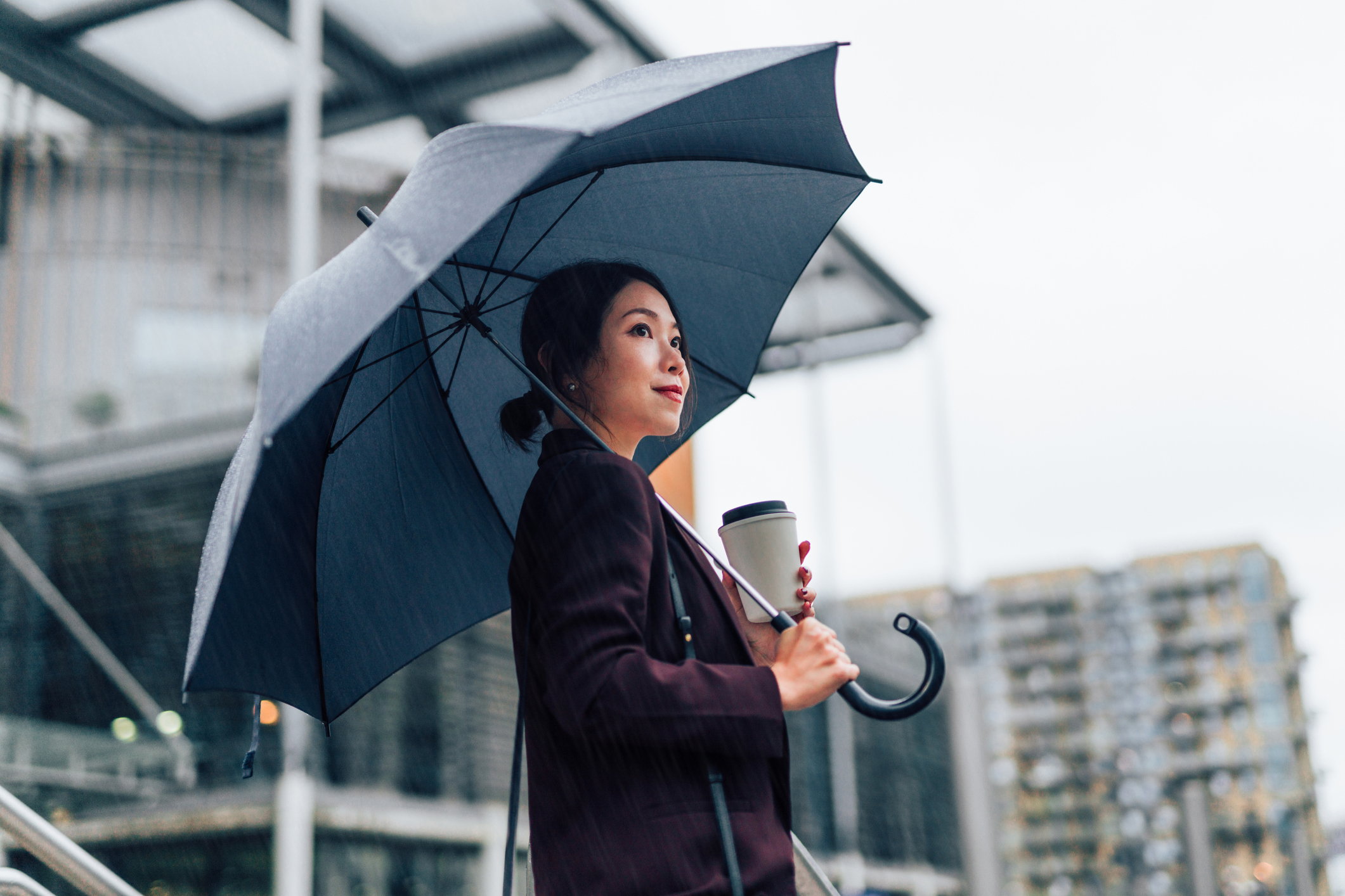 Asian woman holding a coffee and umbrella outside