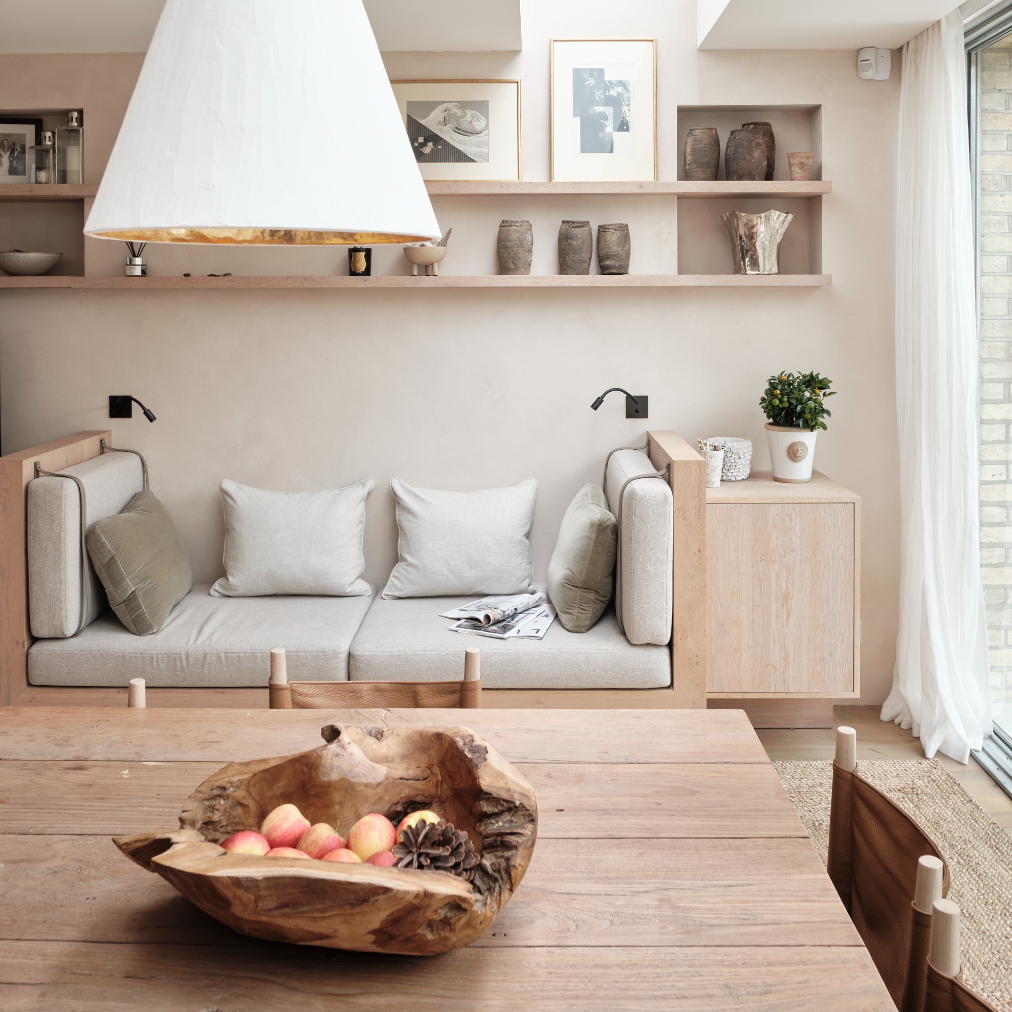 A dining area with a wooden dining table and chairs and a built-in sofa along the wall underneath some floating shelves