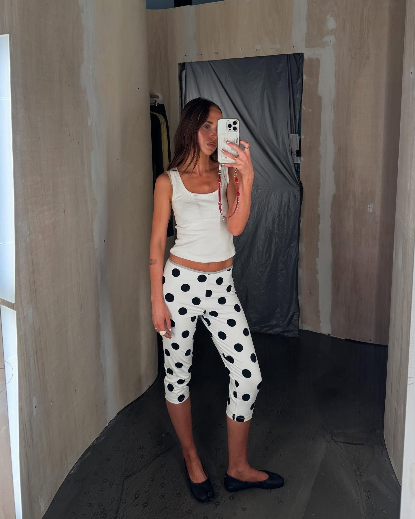Influencer @makenna_alyse takes a mirror selfie wears a white vest top, white capri pants with black polka dots and black ballet flats.