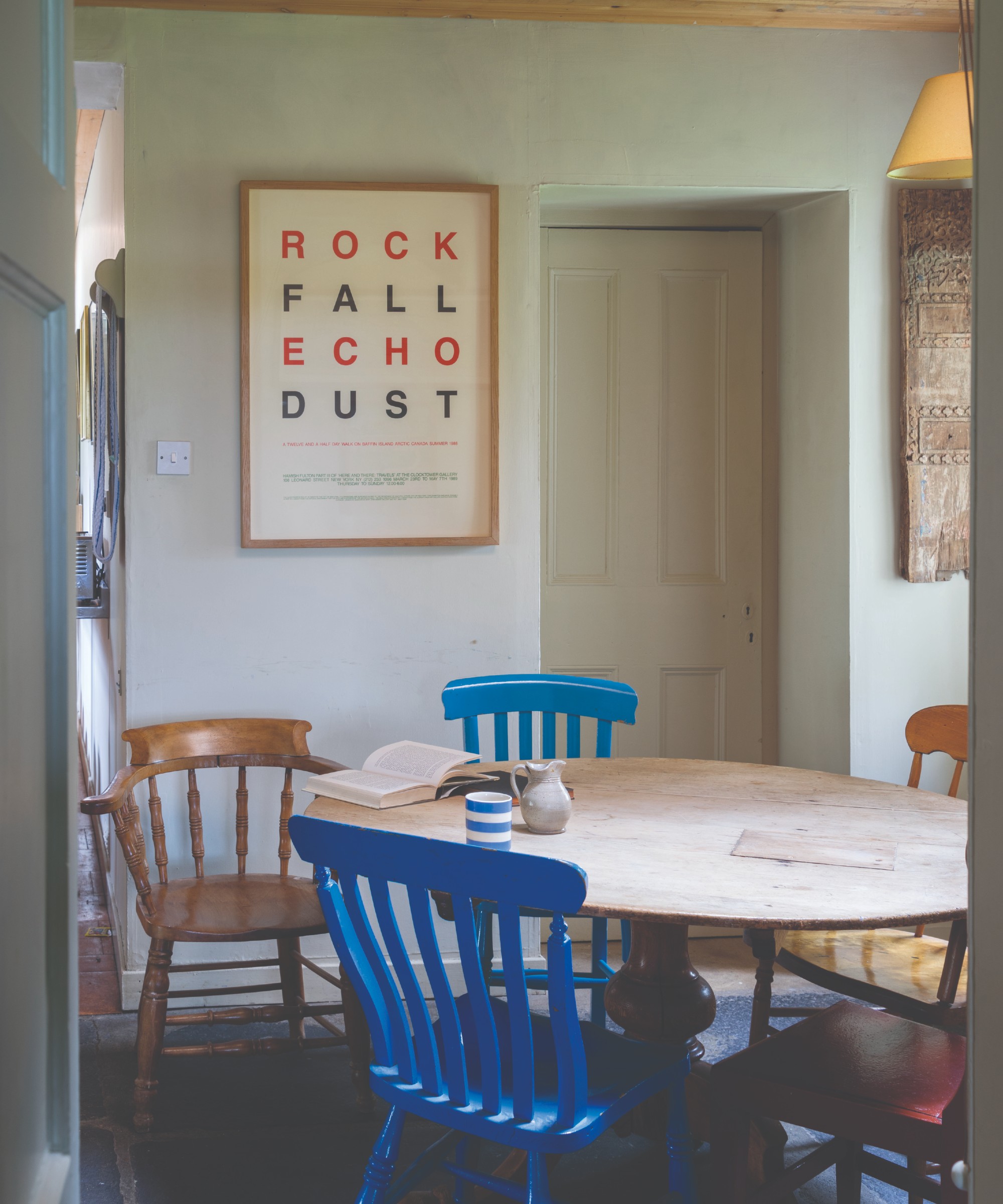A dining room painted in Farrow U Ball's Off-White shade with an oval dining table and two blue chairs