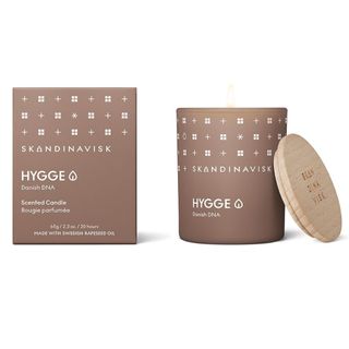 Skandinavisk's scented candle, hygge, in a beige jar with the wooden lid and the candle's packaging on either side