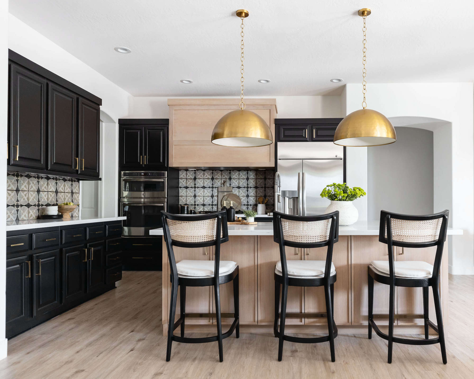 Kitchen with black cabinets and light wood island with pendants over and bar stools