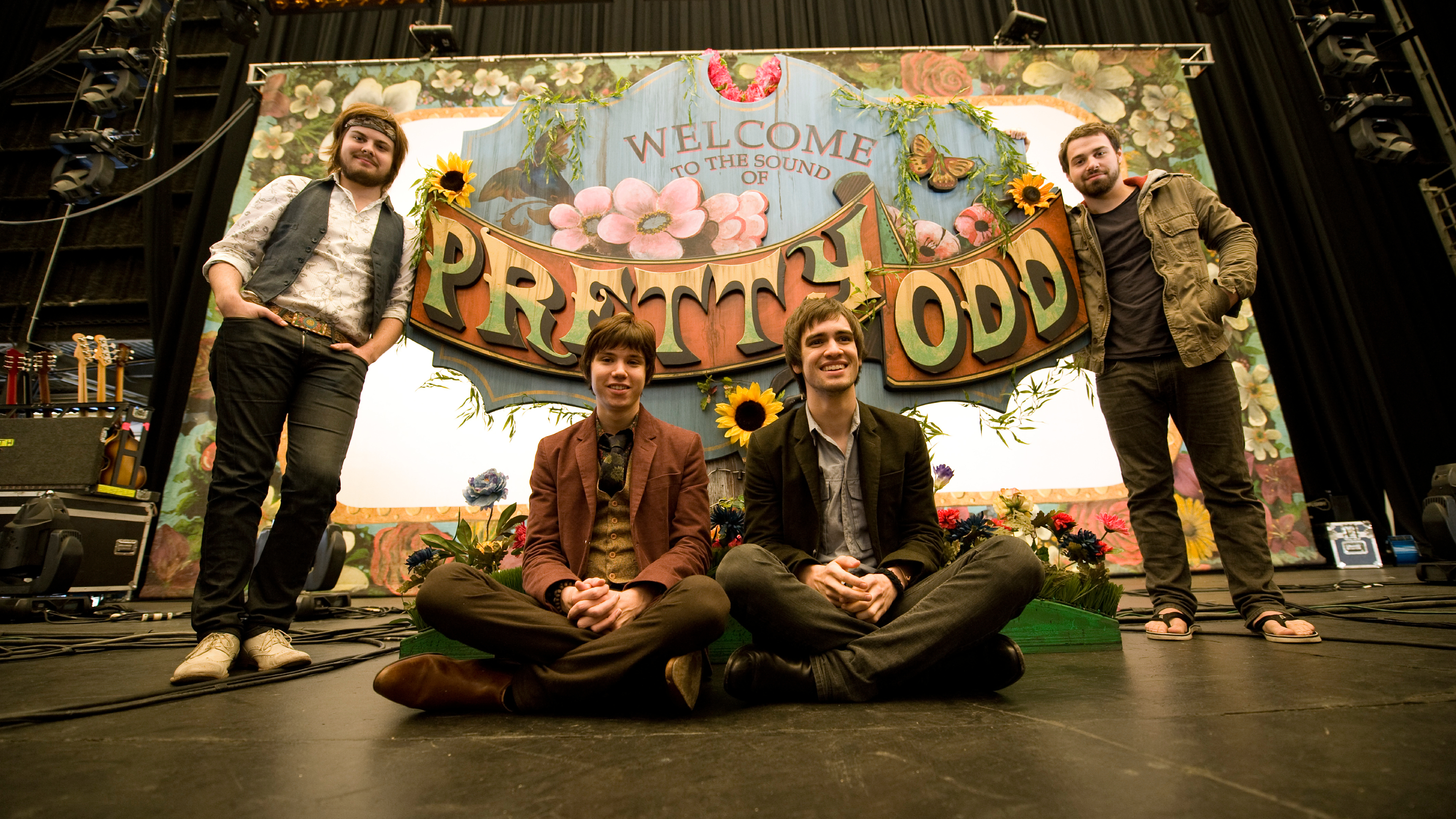 Photo of Panic! At The Disco sitting on stage in front of their tour banner in 2008