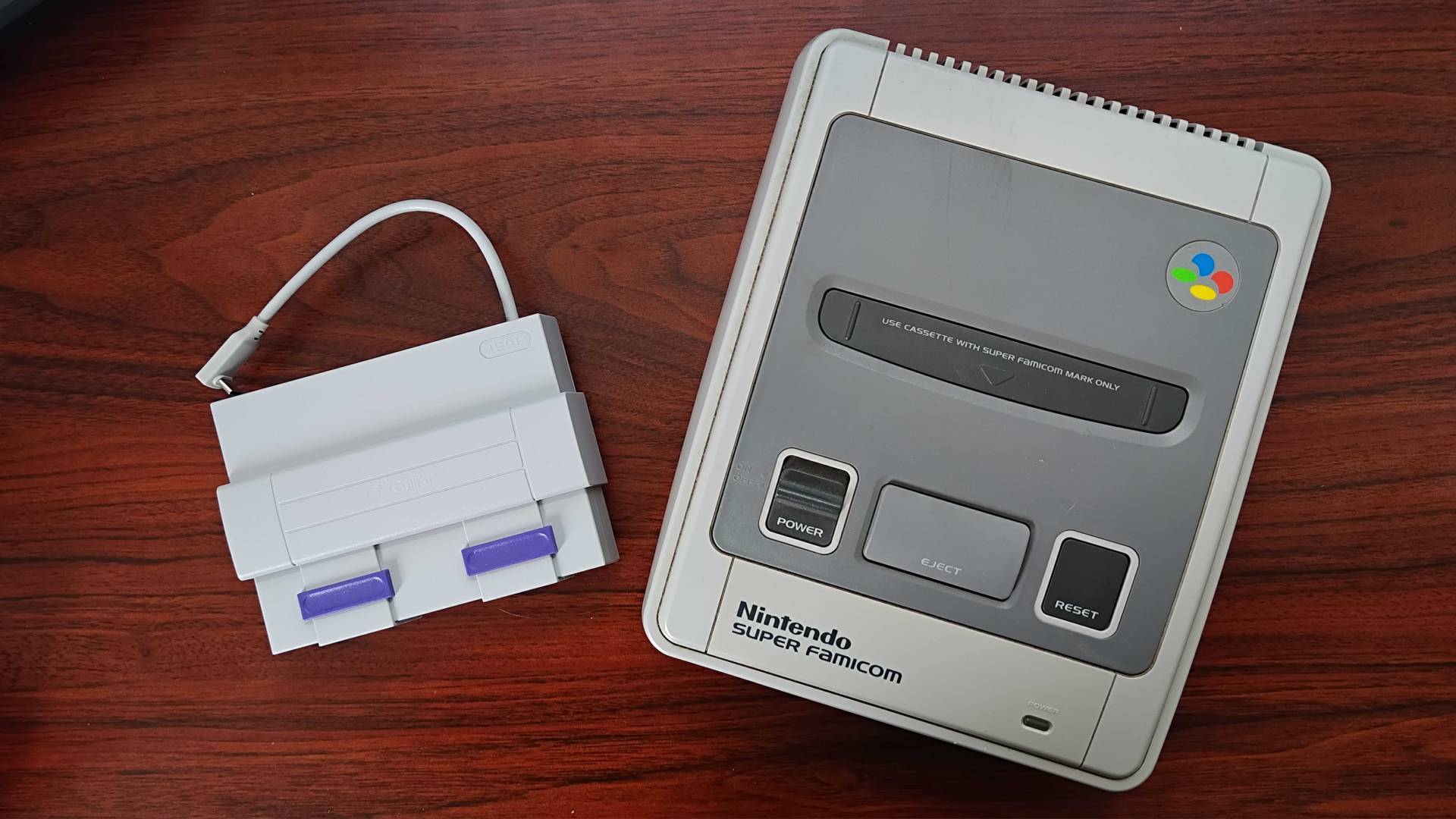 Gulikit Steam Deck dock next to Super Famicom (SNES) on woodgrain desk.