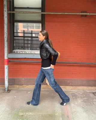 Woman in bootcut jeans and leather jacket.