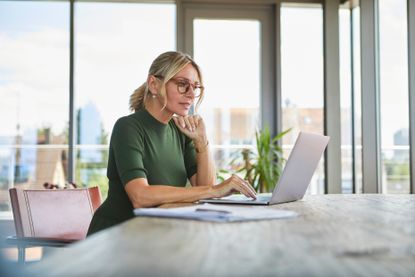 A business woman is working on her laptop at a dining table.