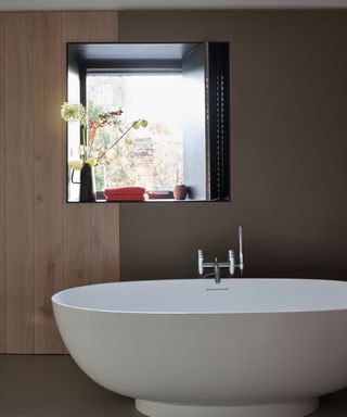 A neutral bathroom with large white tub and square window with vase and flowers