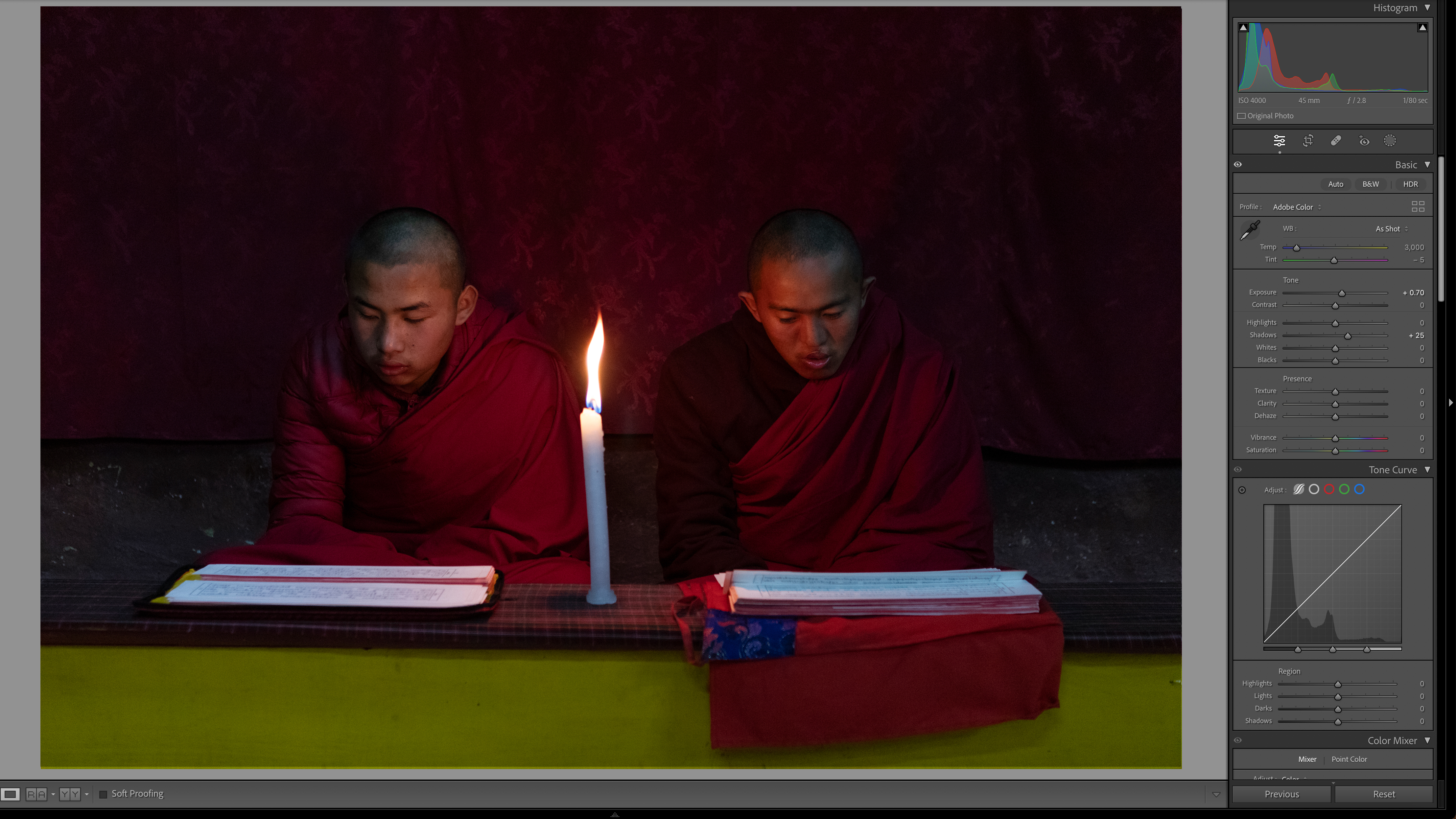 Two individuals in maroon robes are seated side by side, reading by candlelight. The dim setting conveys a calm and meditative atmosphere