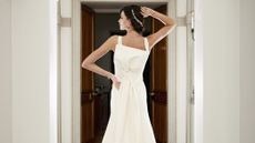 Girl wearing a white wedding dress with a bow, photographed from behind with one arm of her hip and the other on her head