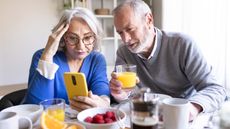 Senior couple reading news on a smartphone while having breakfast