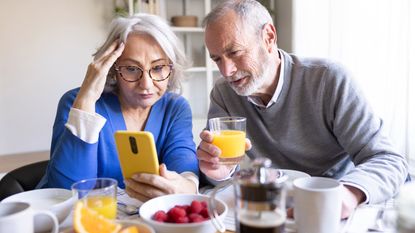 Senior couple reading news on a smartphone while having breakfast
