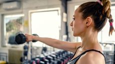 Woman doing a single-arm dumbbell front raise in the gym
