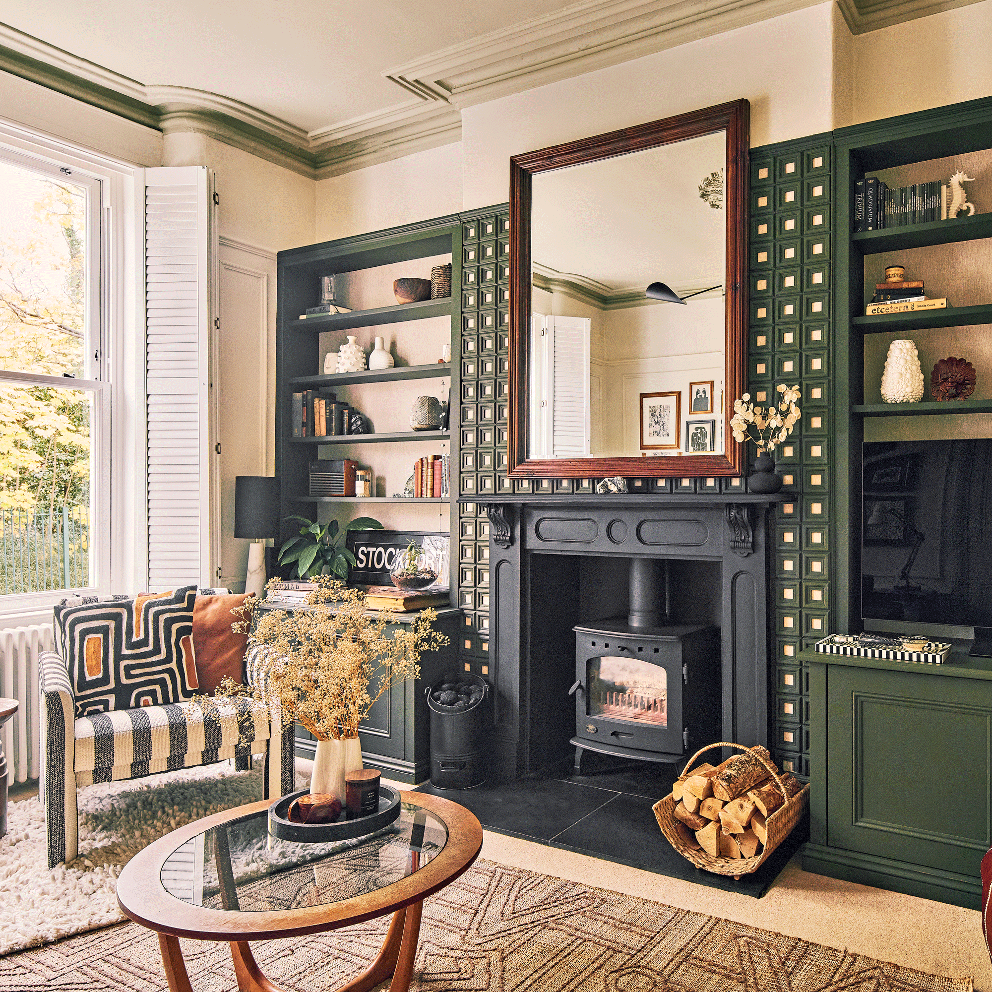 a living room with alcove shelving, fireplace with mantelpiece, large mirror, black and white striped armchair and mid-century style coffee table
