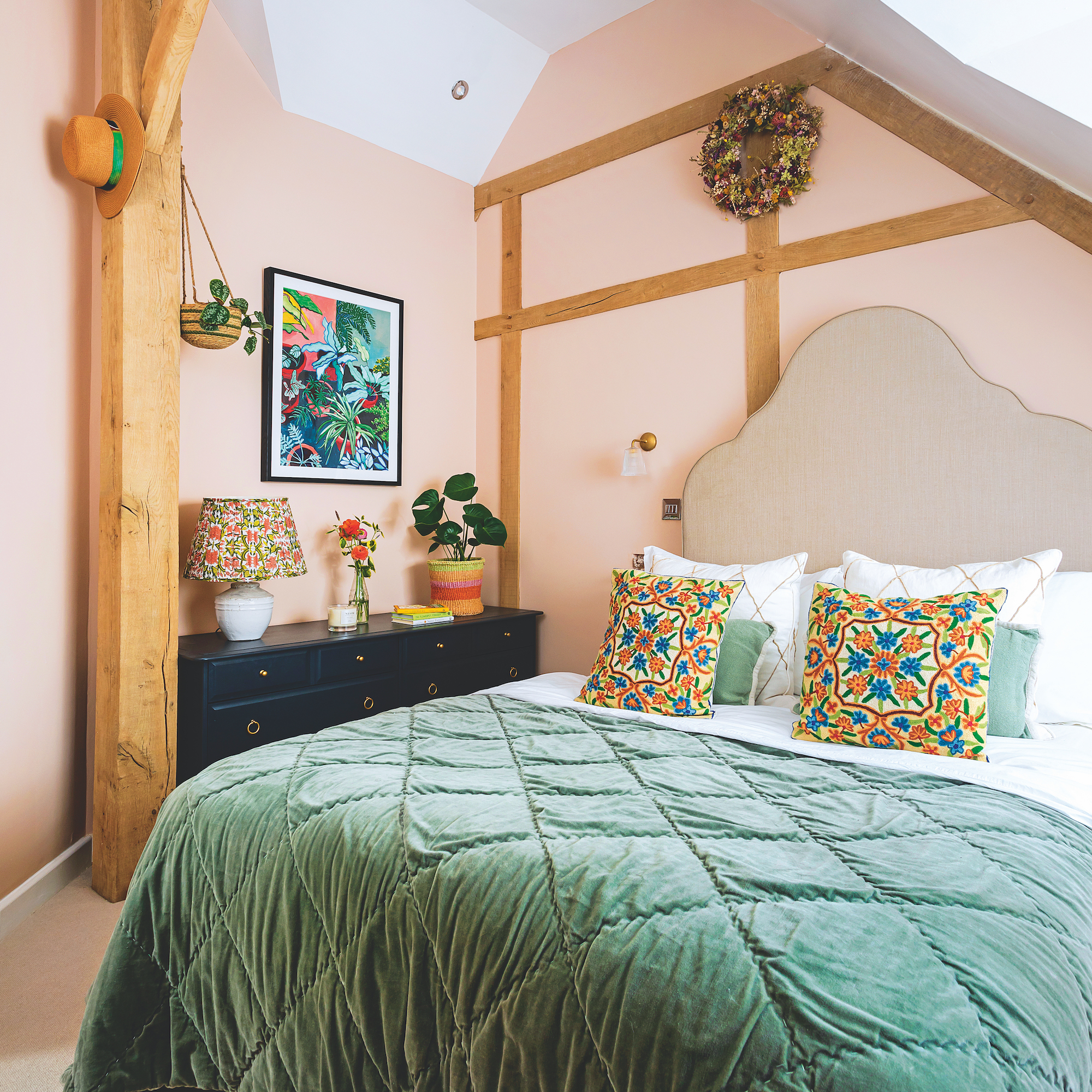 bedroom in oak frame house with walls painted in setting plaster pink by farrow and ball and a green velvet quilt on the bed