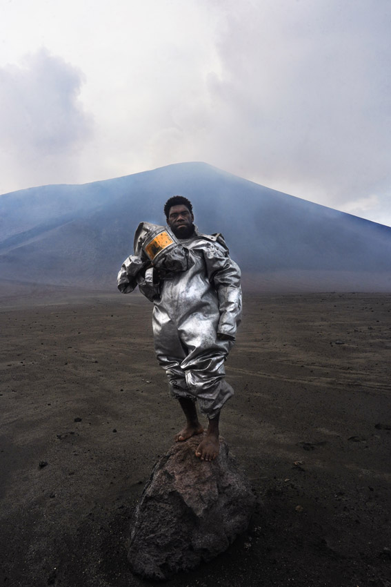 A man dressed in a silver space suit in front of a volcano