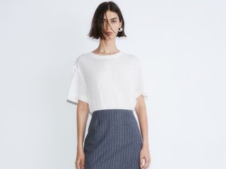 Model wears white t-shirt and pinstriped pencil skirt.