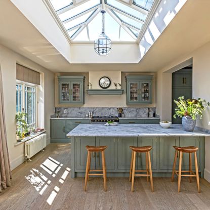 green kitchen cabinetry with sink peninsula and marble worktops