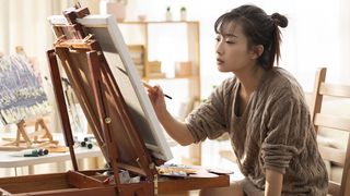 A woman uses one of the best easels for painting in a studio applying her brush.