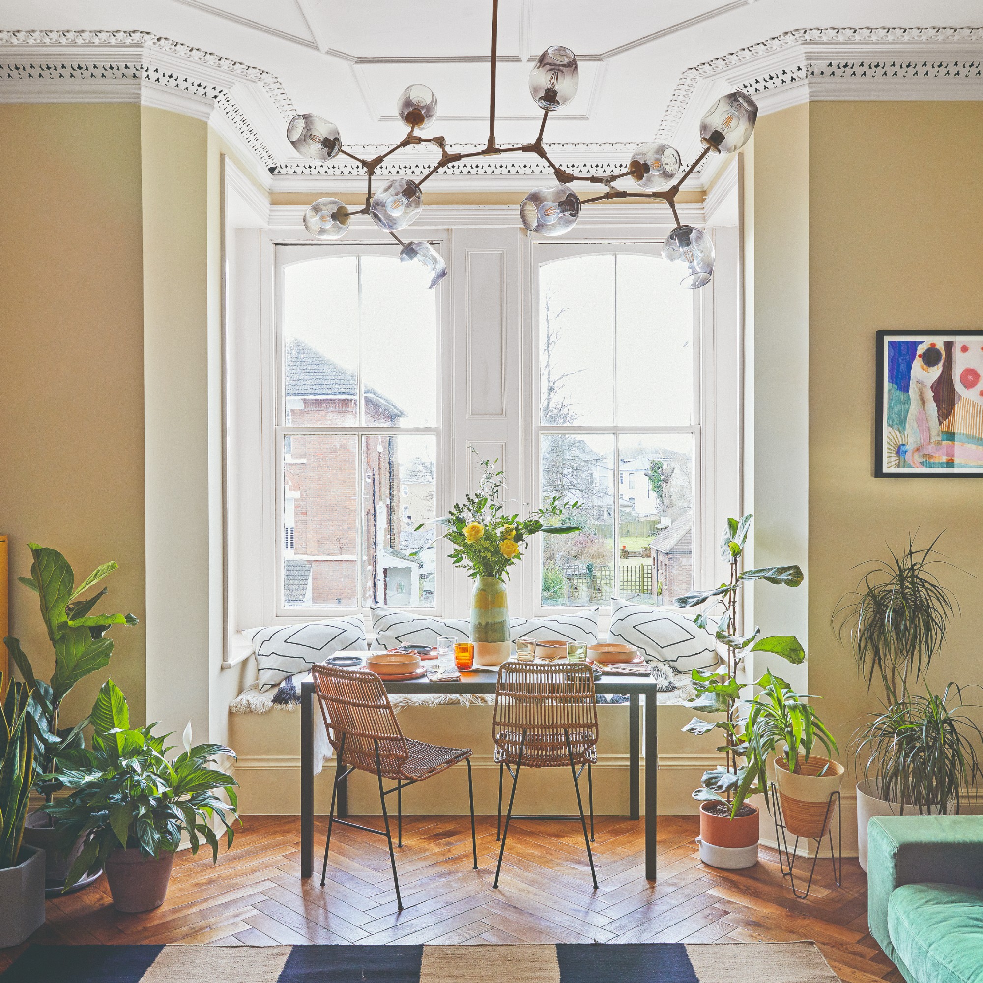 A butter yellow-painted living room with a dining window nook and a modern sculptural chandelier