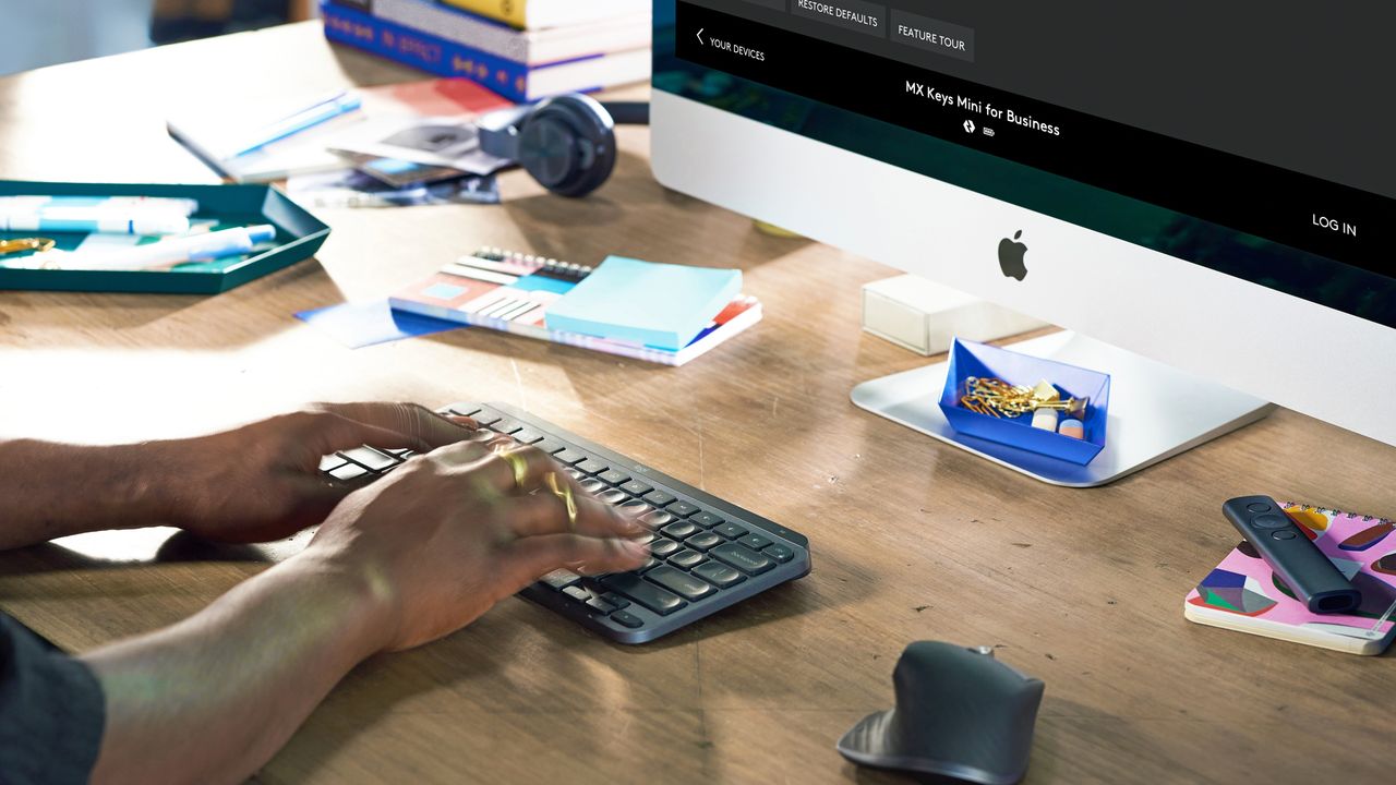 Logitech MX Keys Mini being used on large wooden desk in front of Mac