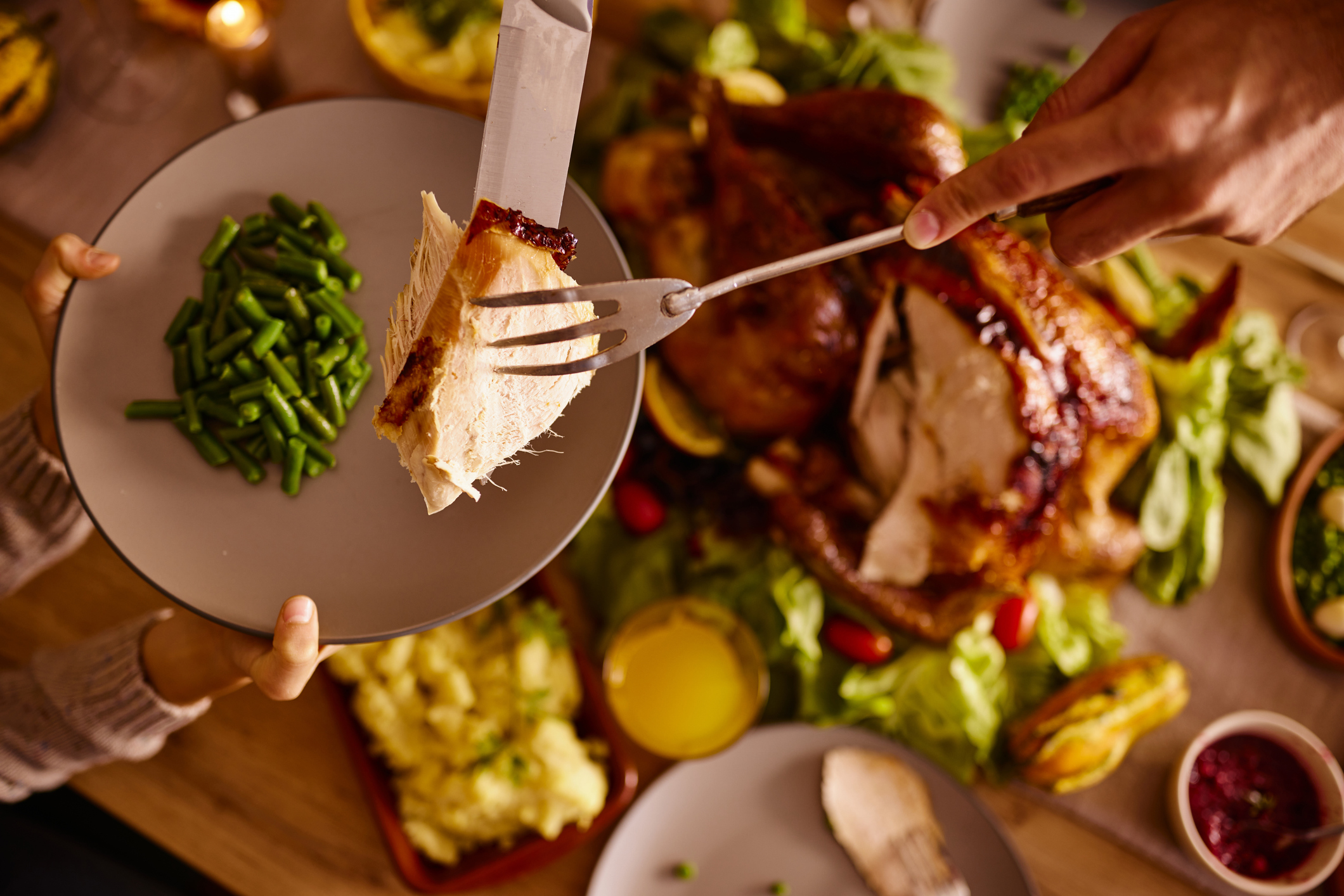 Close up of unrecognizable father serving slice of turkey meat to his child during Thanksgiving lunch at dining table.