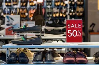 50% off sale sign on a shop shelve, surrounded by a display of men's shoes