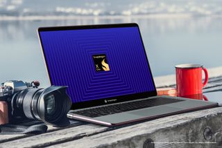 Qualcomm Snapdragon X Elite reference design laptop on a bench with a camera and coffee mug