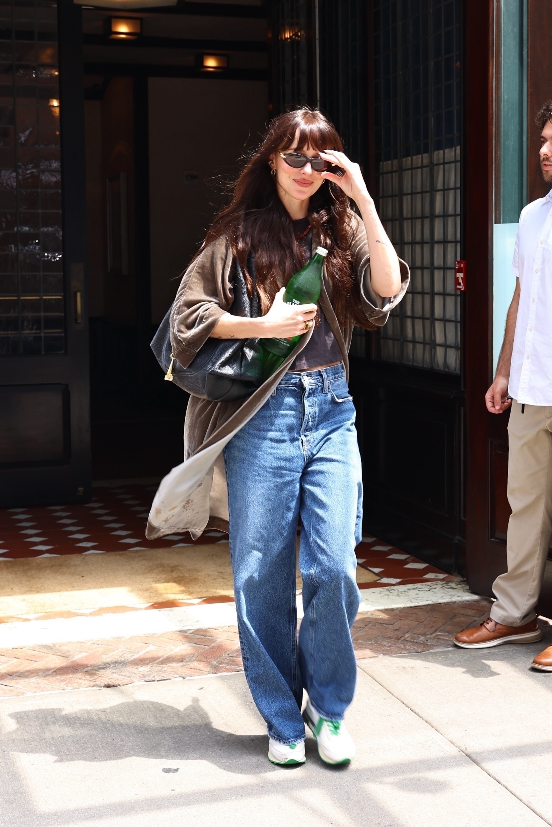 Dakota Johnson wears baggy jeans, white and green sneakers, and sunglasses