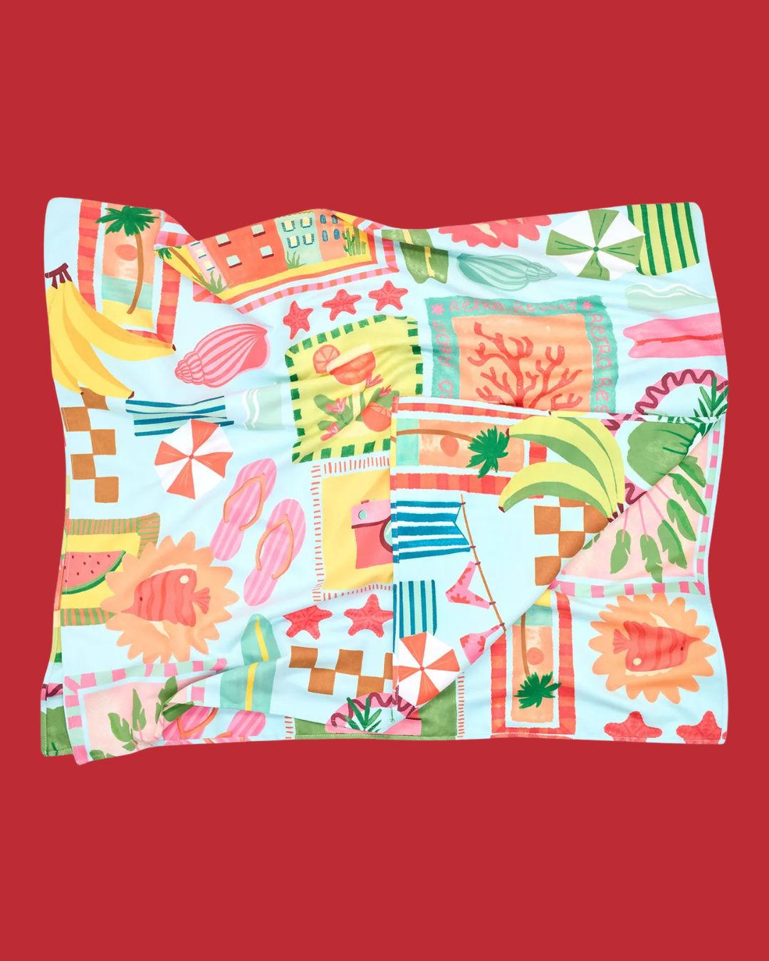 A microfiber beach towel with a pale blue background and lots of summery motifs, from tropical fruits and parasols to flip flops and more, scattered across its surface, placed against red background.