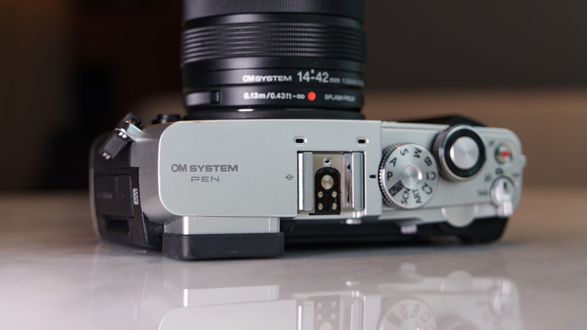 Close up of the OM System PEN mirrorless camera's top plate, in a modern room