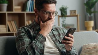 Caucasian adult man male guy at home living room nervous looking at mobile phone.