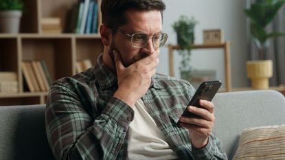 Caucasian adult man male guy at home living room nervous looking at mobile phone.