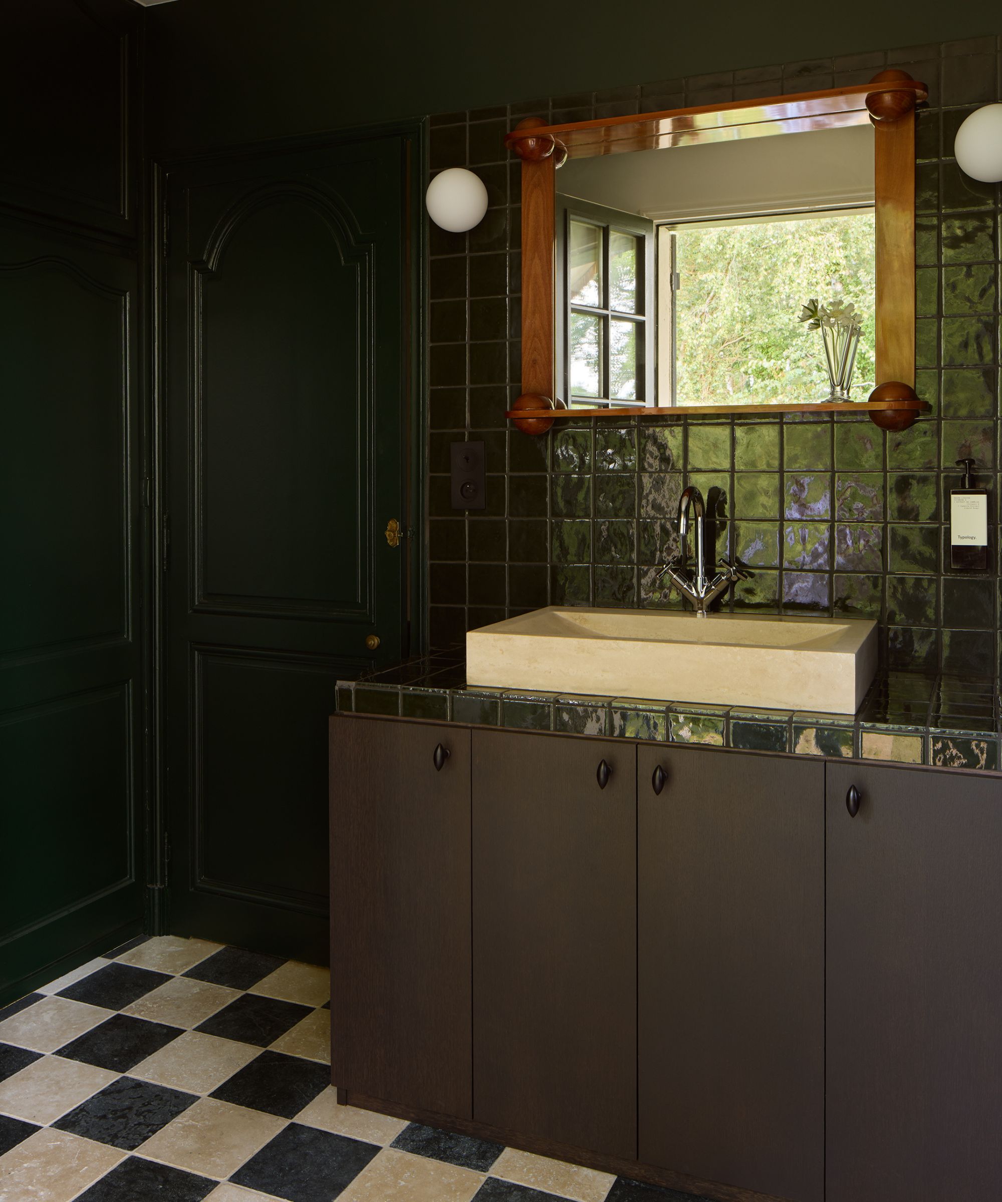 a dark green bathroom with zellige tiles, painted doors, chocolate rown vanity and a checkerboard floor