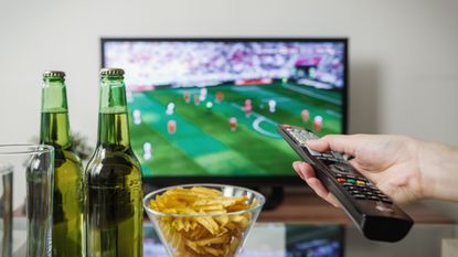 The best OLED TVs: Image depicts hand with remote, beer and chips on coffee table in front of TV