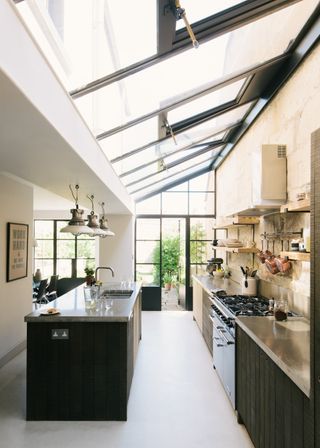 A glass roof in a small kitchen extension. In the kitchen is a black colored island mirroring black lower cabinets. Above the island are three pendant lights.