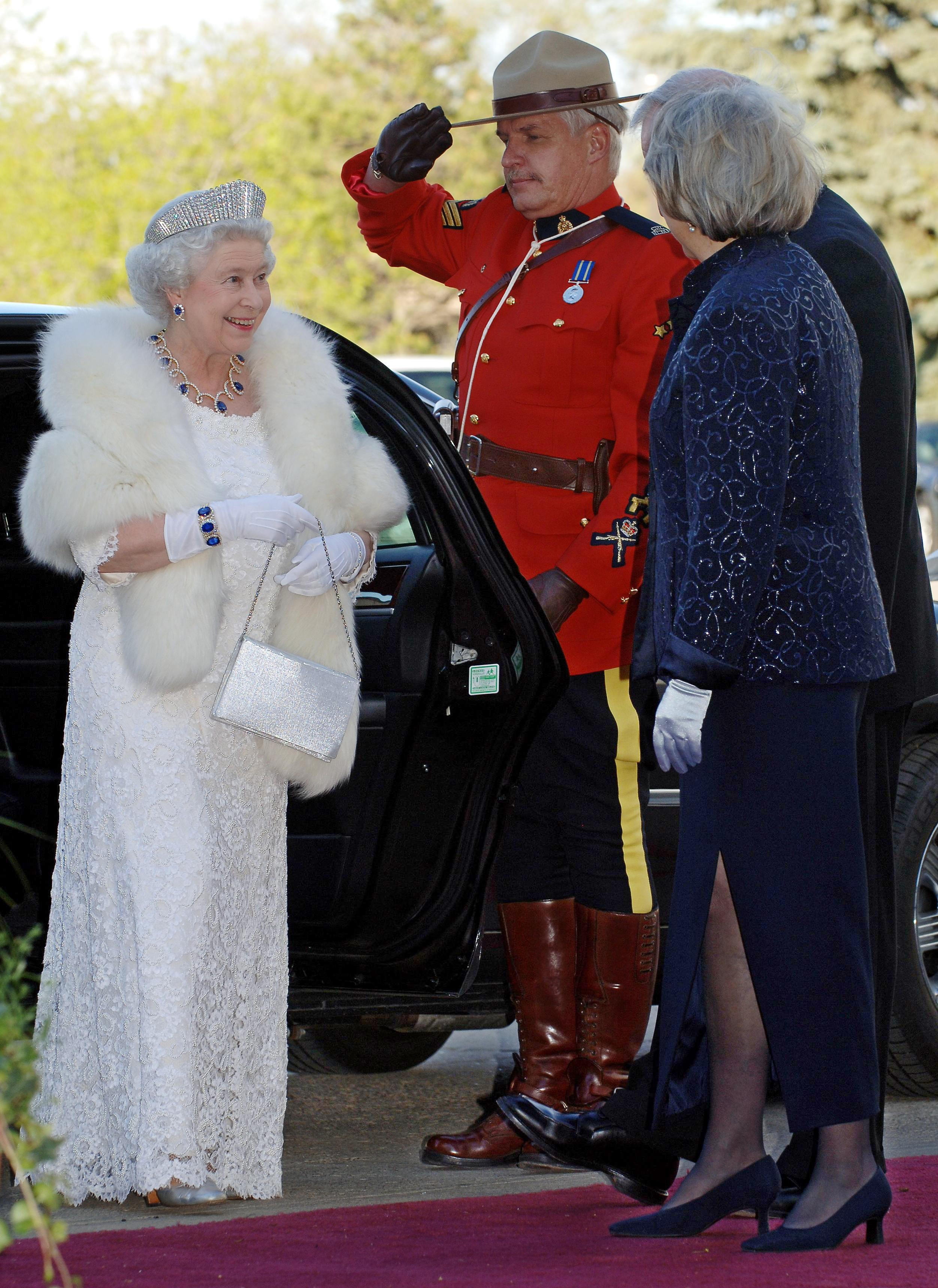 Queen Elizabeth wearing a fur stole, white dress and tiara getting out of a car