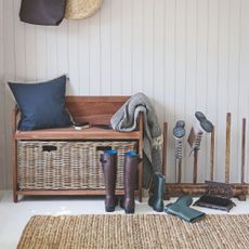 hallway with a storage bench covered in cushions and throws, next to boots on the floor and on a boot rack