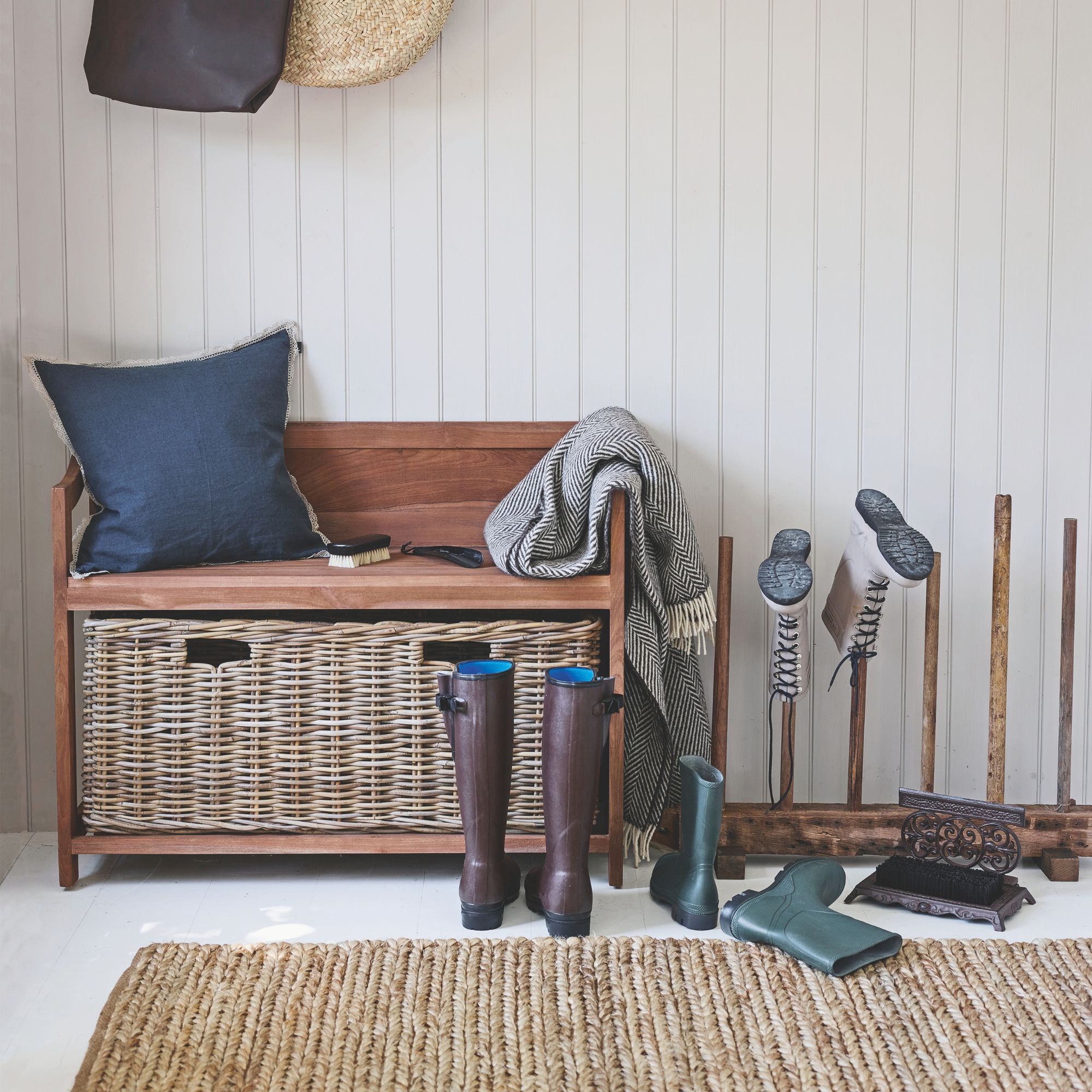 hallway with a storage bench covered in cushions and throws, next to boots on the floor and on a boot rack