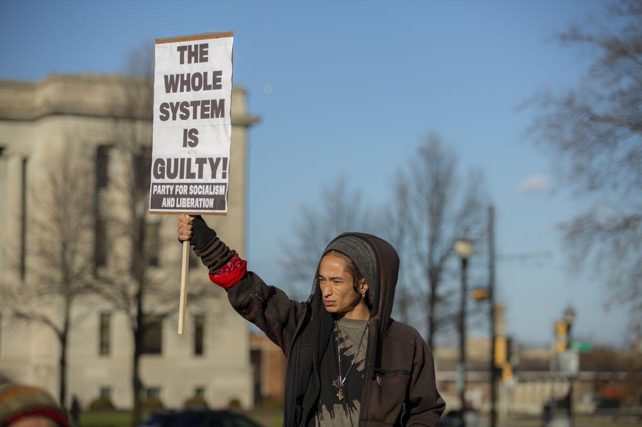 Person holds sign reading &amp;#039;the whole system is guilty!&amp;#039;