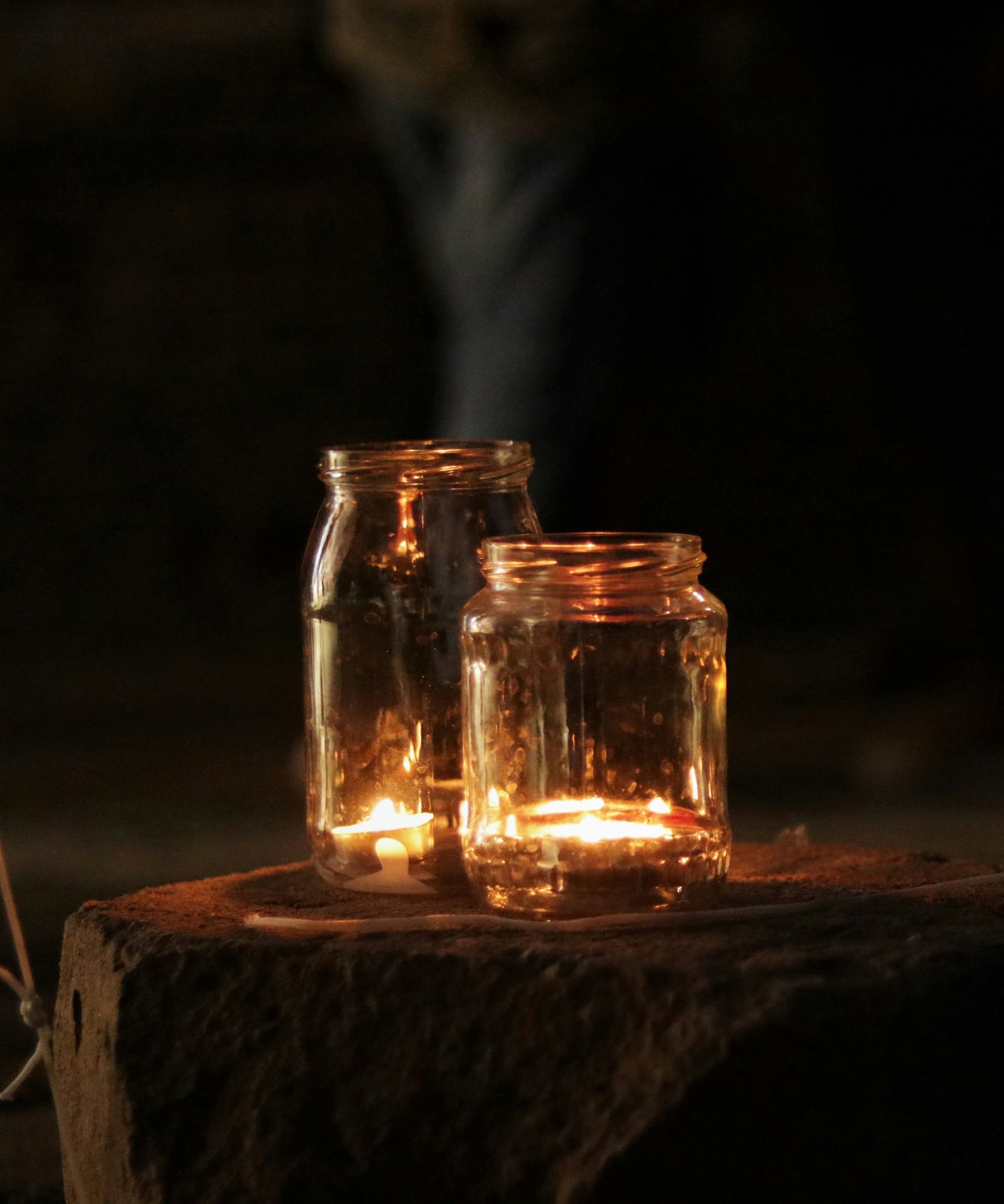 Two large mason jars with tea lights inside, sitting on a stone slab at dusk