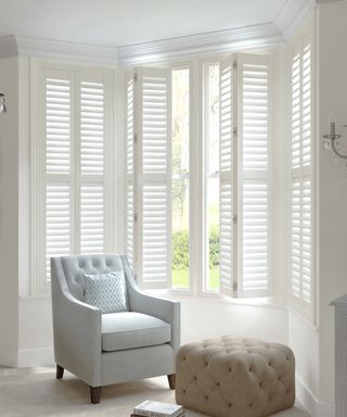 White window shutters with smart armchair and buttoned pouffe.