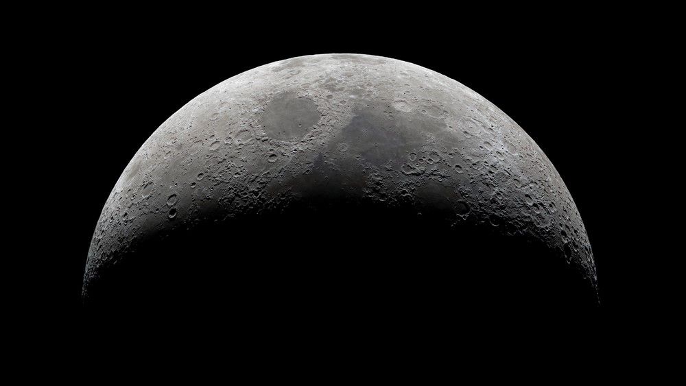 A black and white photo of the moon. The top is bathed in light.