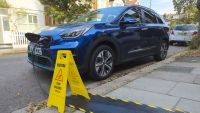 Kia electric car charging on a residential street from house using pavement cable protectors for the EV charging cable