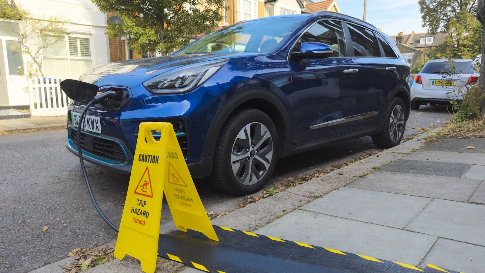 Kia electric car charging on a residential street from house using pavement cable protectors for the EV charging cable